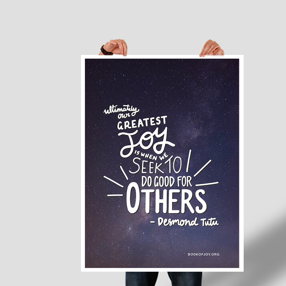 A picture of somebody, likely a white man, holding up a large poster the size of a standard human body, saying in handlettering against a milkyway sky a quote from Desmond Tutu that ultimately our greatest joy is when we seek to do good for others.