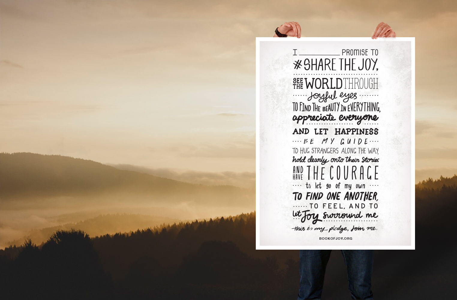 A person is holding a large white posters with the lettering I [insert name] promise to share the joy, see the world through joyful eyes, to find the beauty in everything, appreciate everyone, and let happiness be my guide. To hug strangers along the way, hold dearly onto their stories, and have the courage to let go of my own. To find another, to feel, and to let joy surround me. This is my pledge, join me.