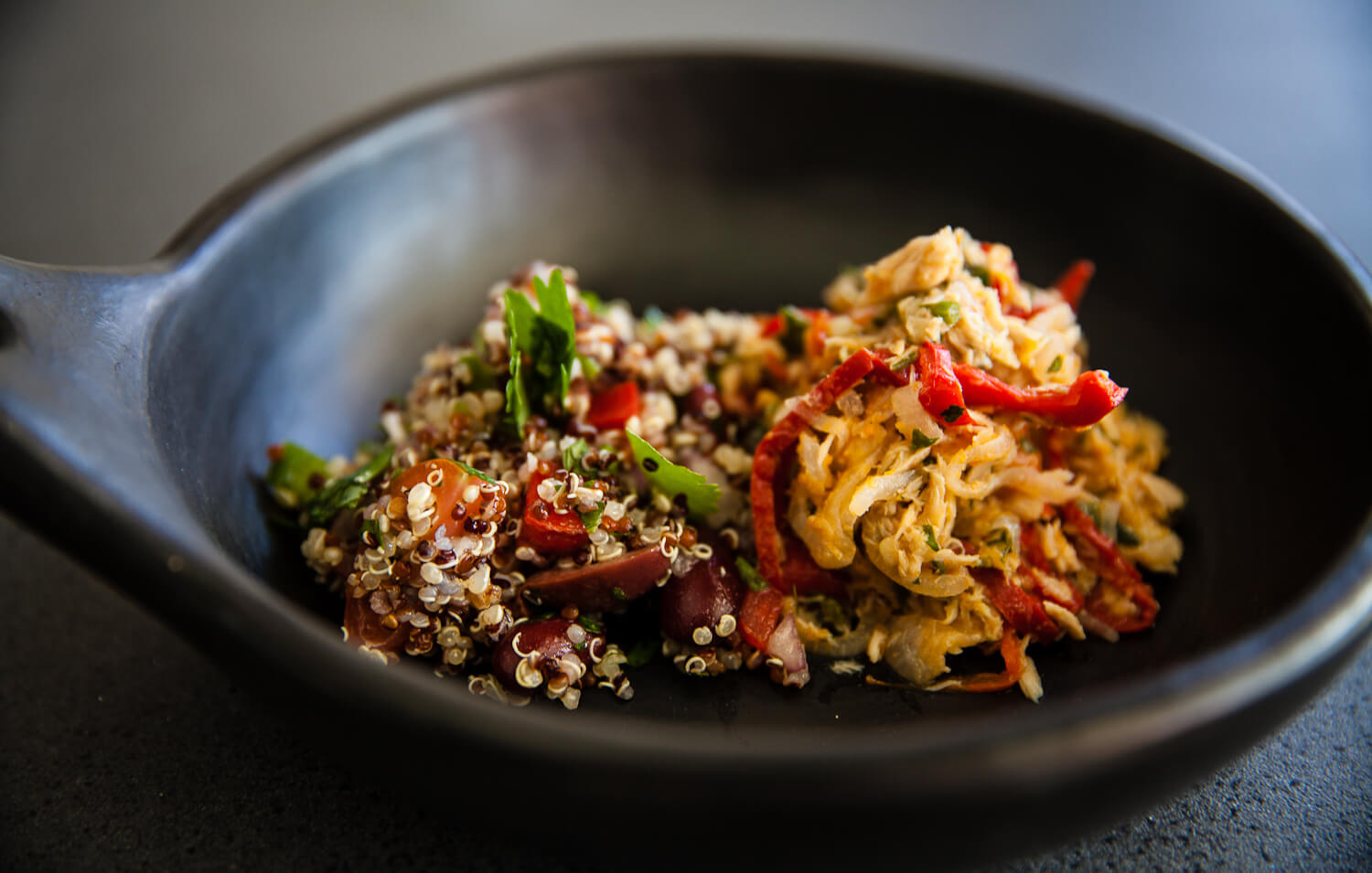 A beautiful closeup photo of an extra large slate grey serving spoon filled with a quinoa and chicken salad