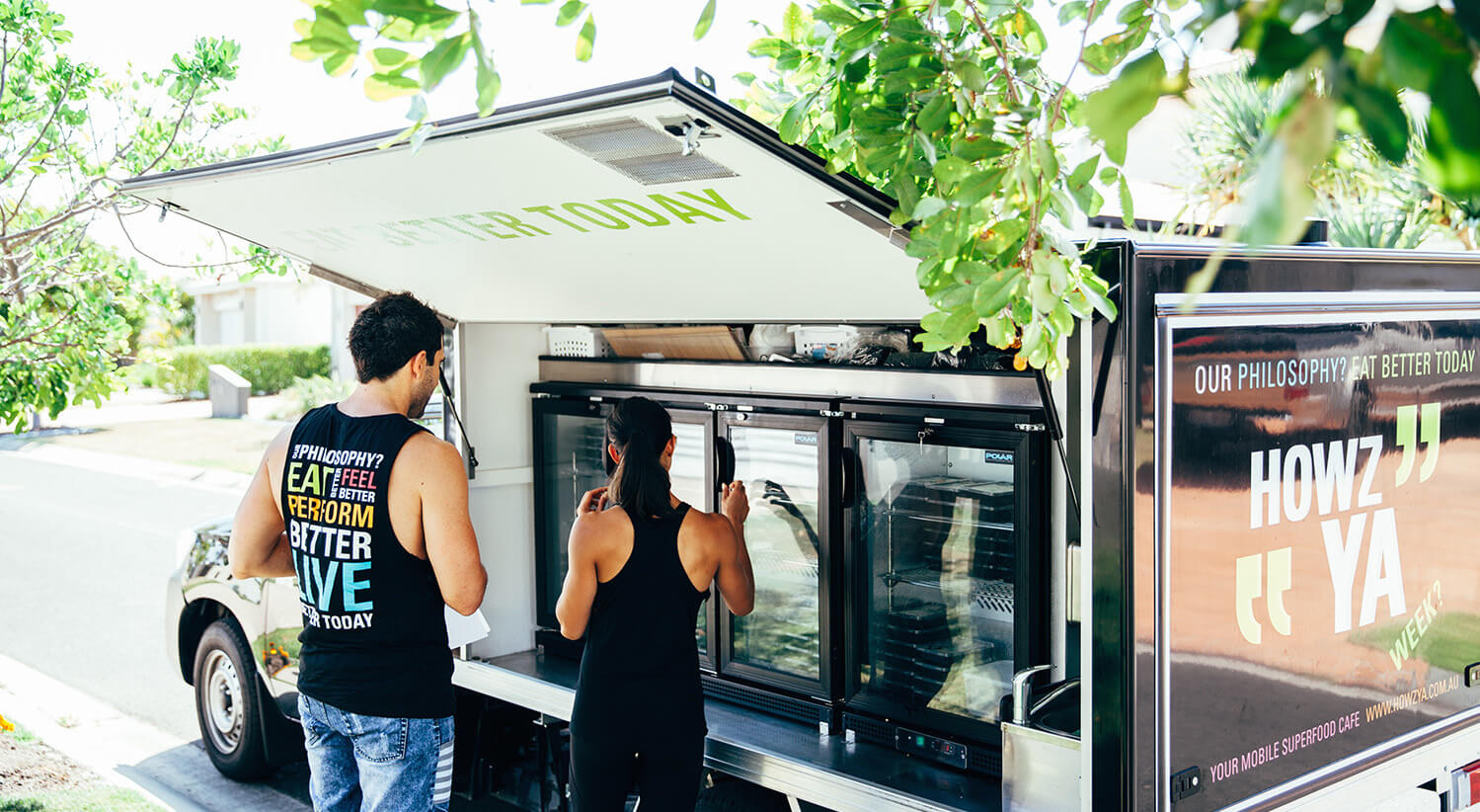 The two founders at their food truck that they used for meal delivery, markets, and events underneath a big tree