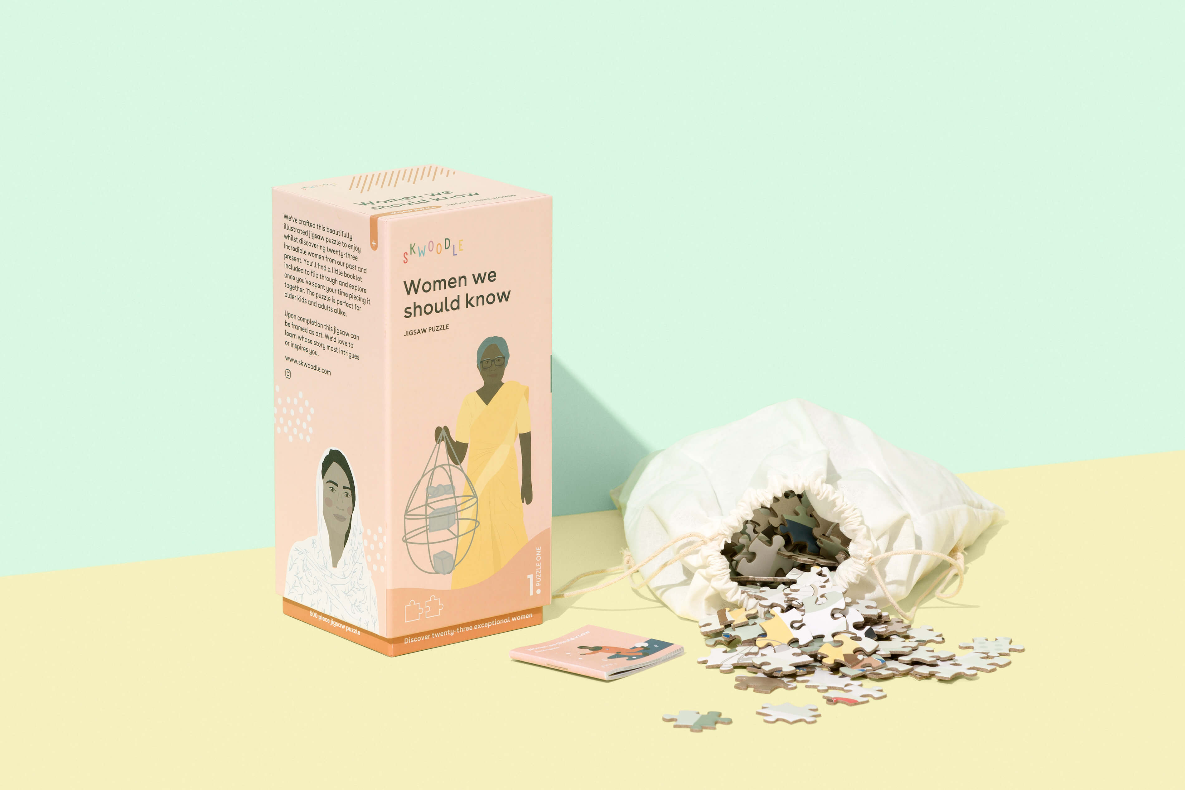 The manufactured puzzle box has been photographed professionally against a green and yellow background. The puzzle stands on the yellow floor with the booklet laying in front, and the white cotton bag next to it on the right, with the puzzle pieces spilling out.